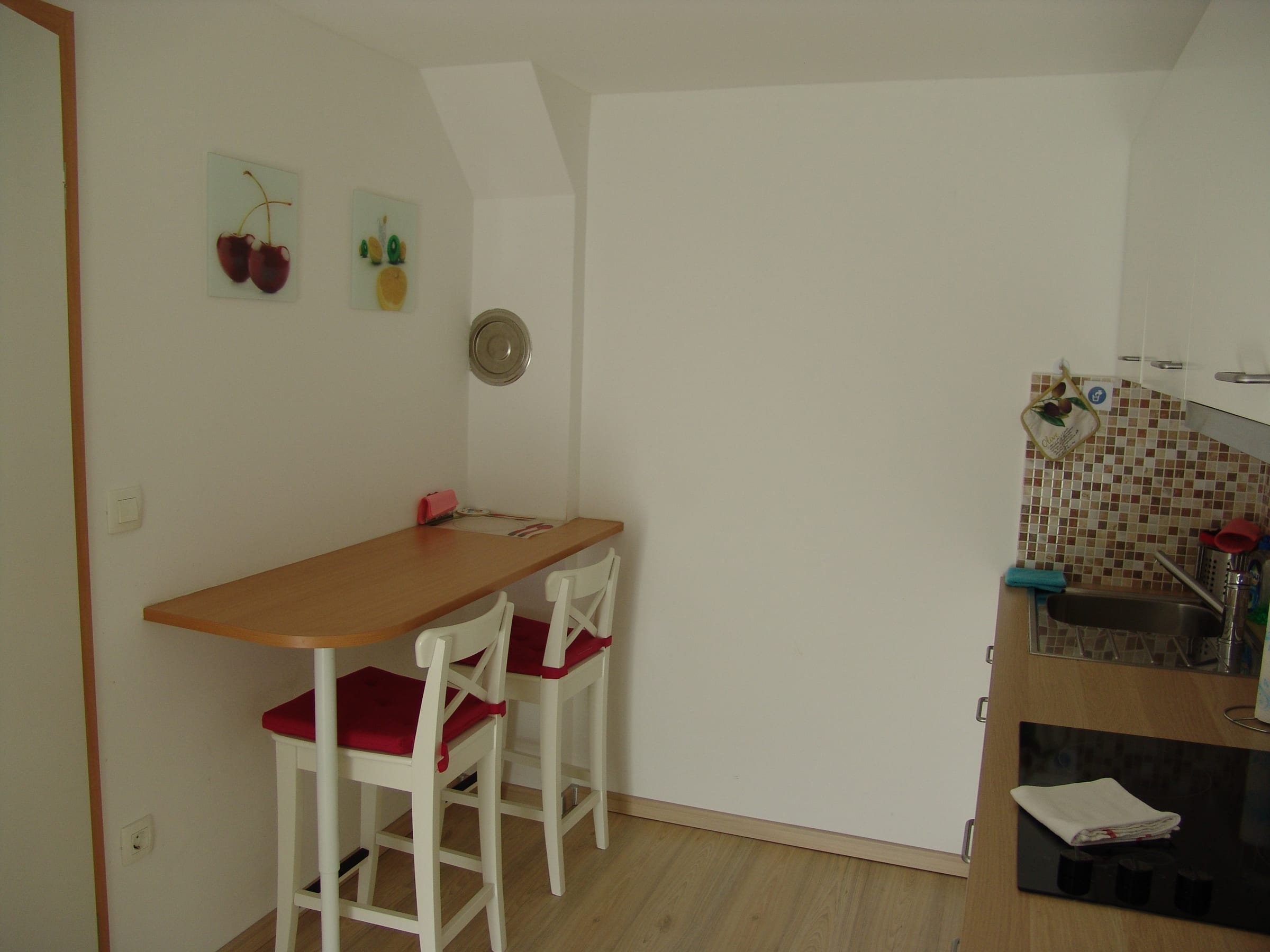A wooden breakfast counter with two red-cushioned stools set against a tiled wall.