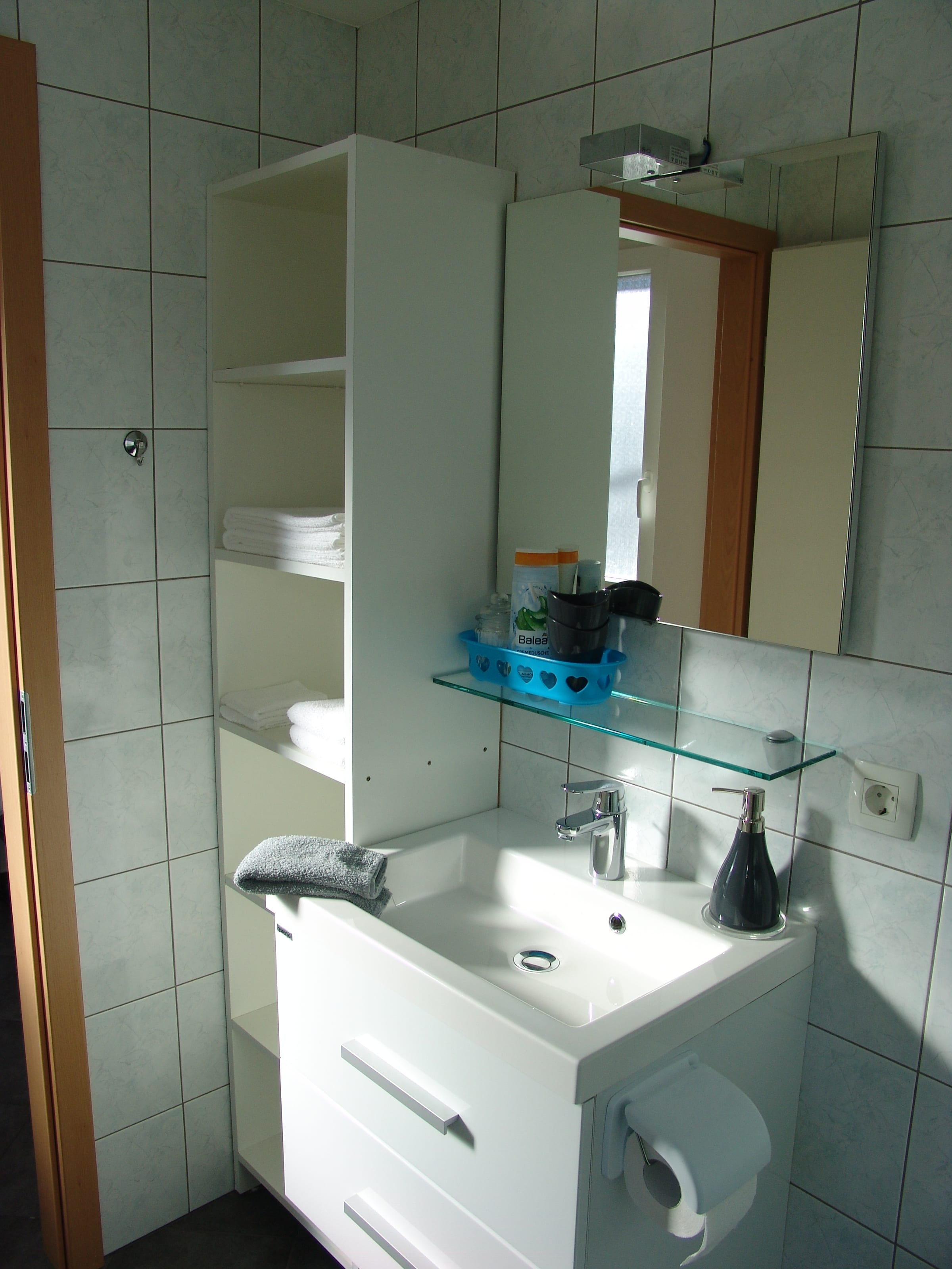 Washbasin with a mirror above it and folded towels on a glass shelf.
