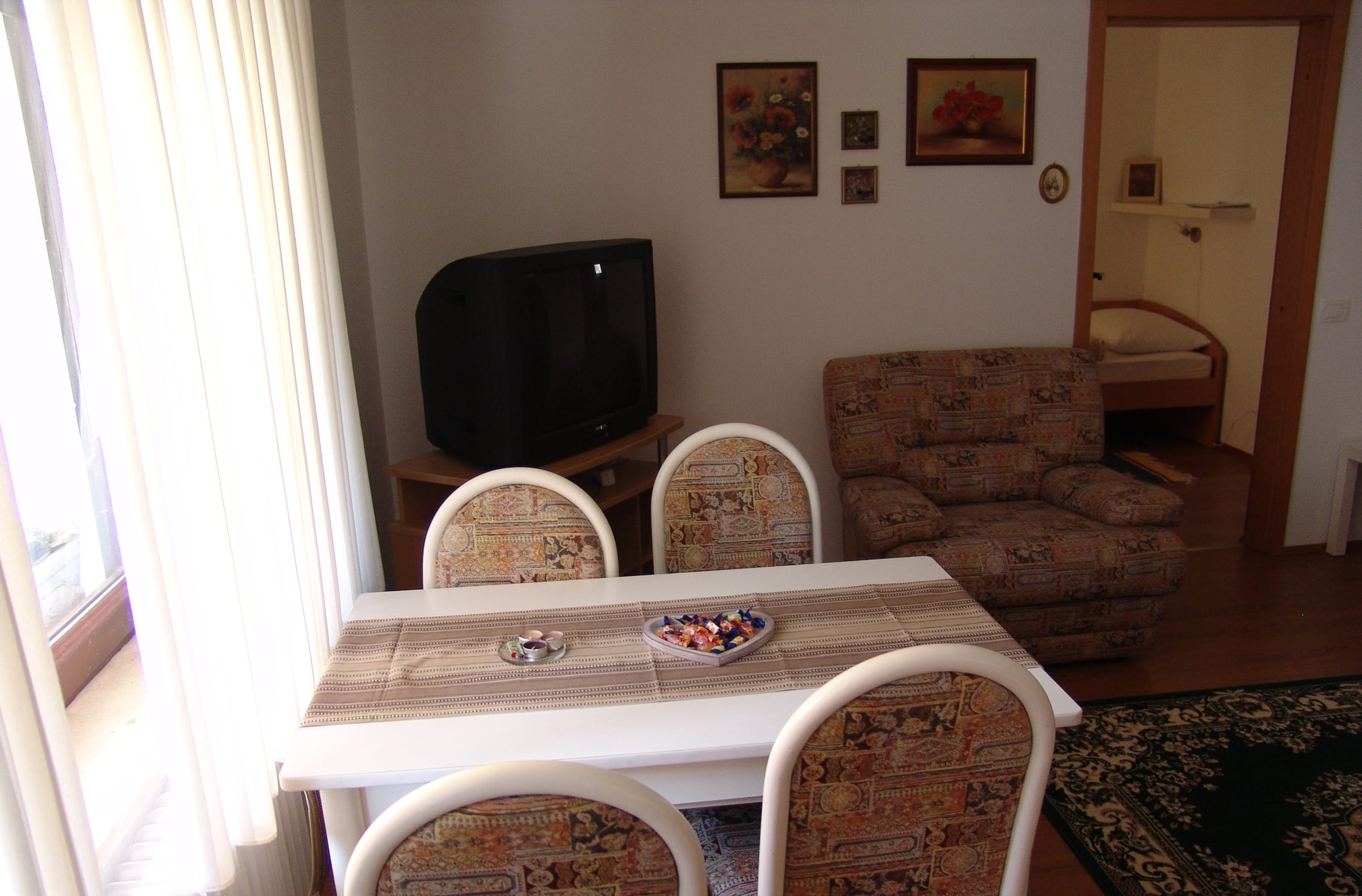 A dining table and chairs by the window, with a television and an interior door beyond.