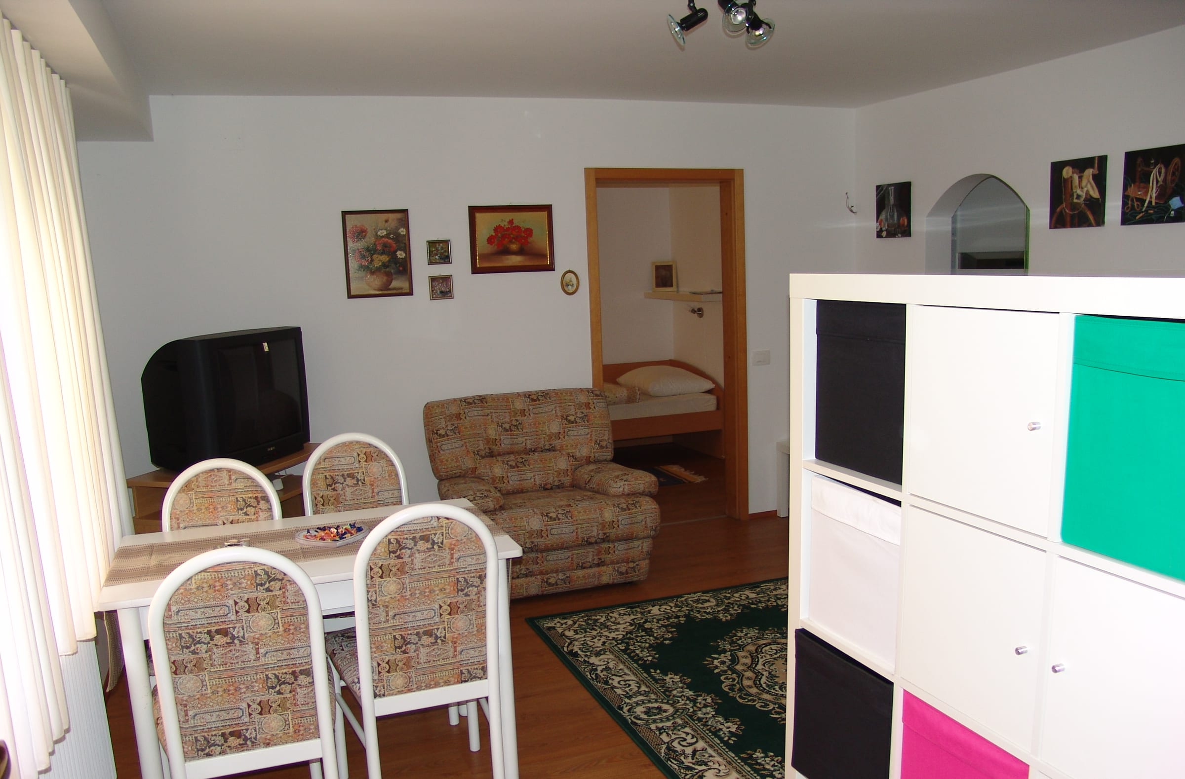 A sitting room with a dining table, a sofa and a white and coloured storage unit.