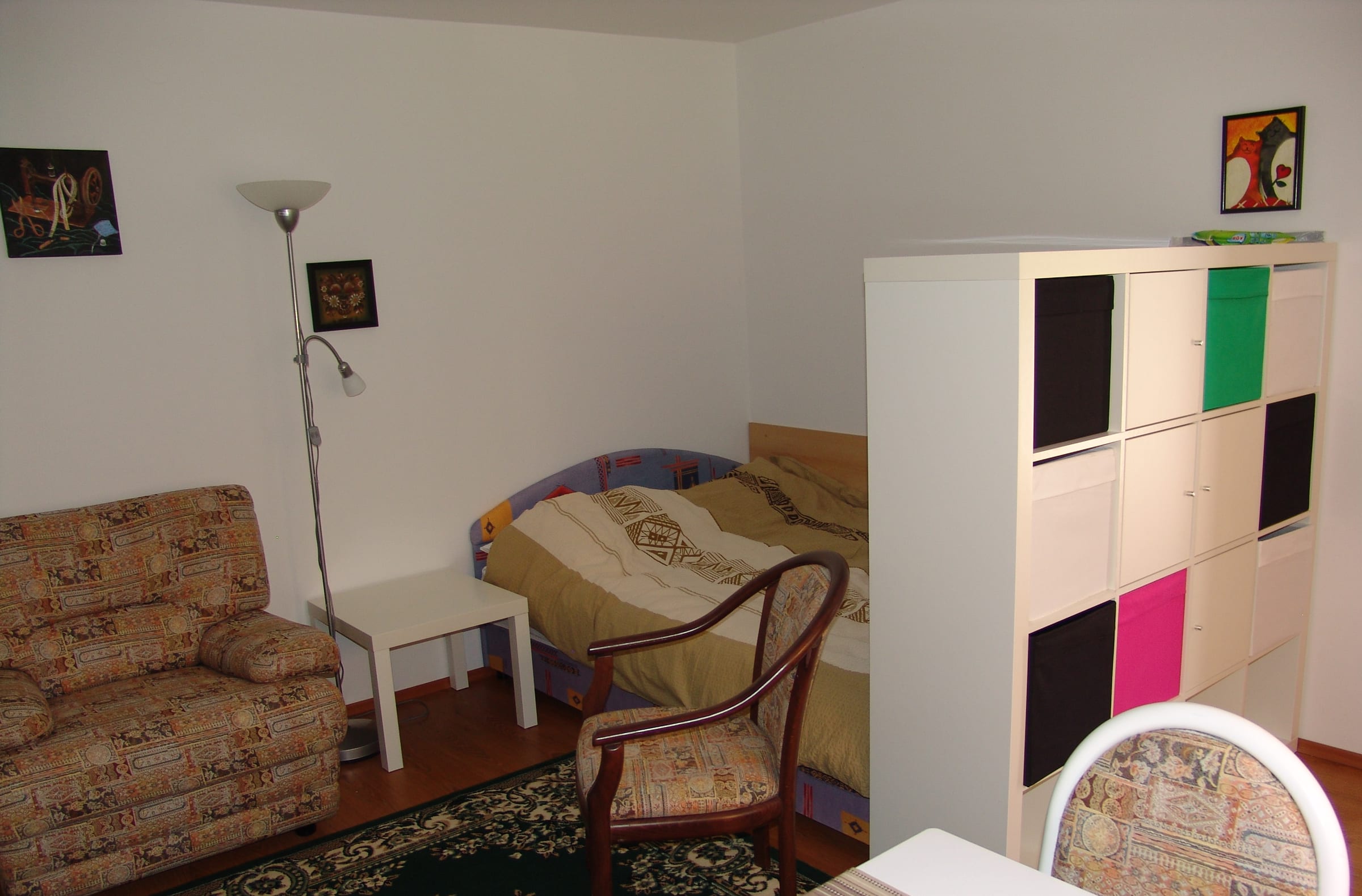 A corner sofa and armchair beside a tall storage unit with coloured drawer fronts.