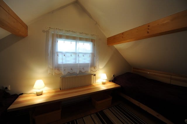An upper-floor bedroom under a sloping pine ceiling, lit by bedside lamps beside a shuttered window.