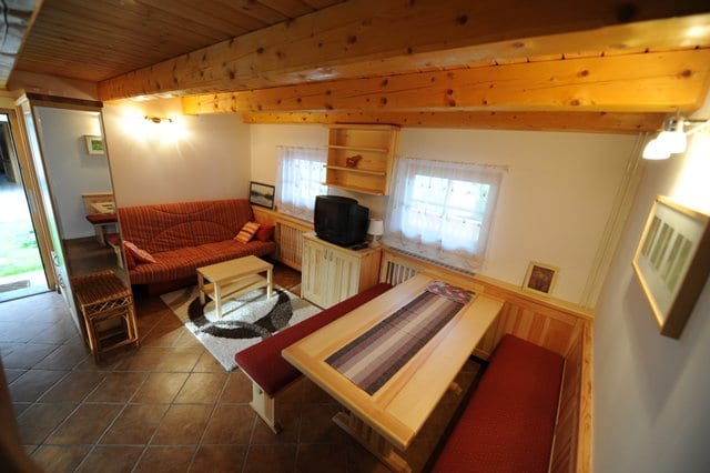 Living and dining room inside the cabin, with a pine ceiling, a dining table, bench seating and a television.