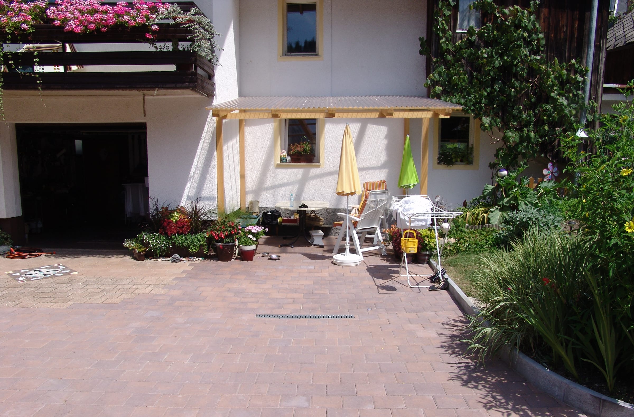 The paved courtyard beside the house, with a timber pergola and planting along the edge.